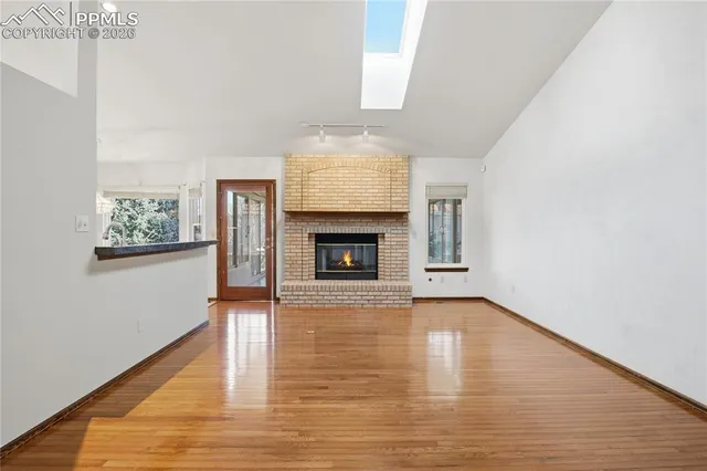 a view of an empty room with wooden floor fireplace and a window