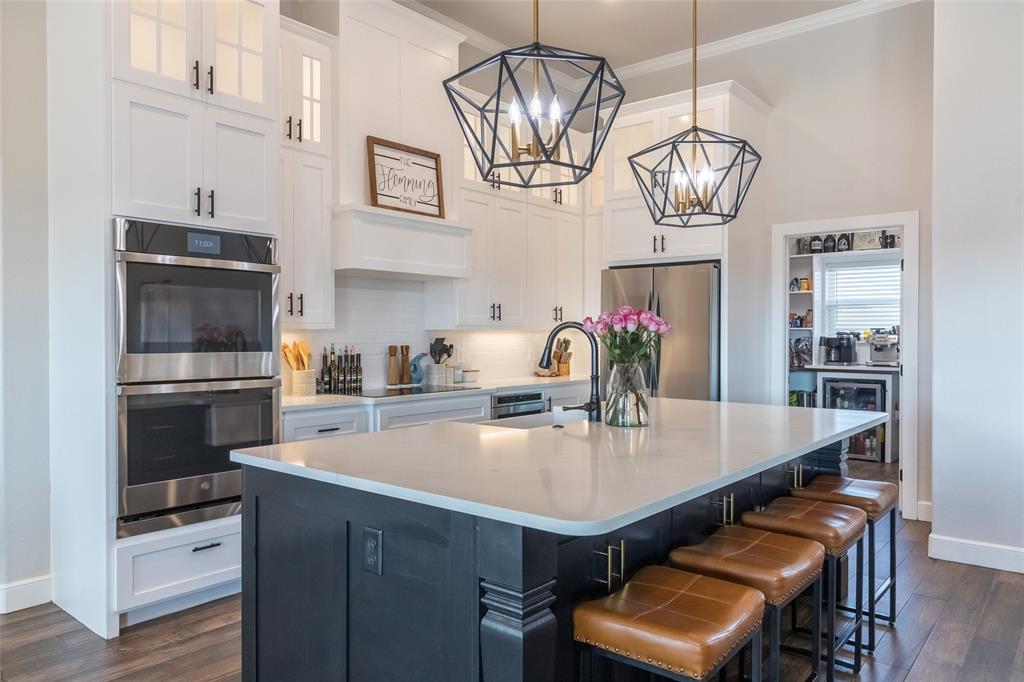 107 Kleingrass Road Abilene, TX 79606 - Photo 5 of 33 Open-concept kitchen featuring an expansive island with seating, built-in stainless steel double ovens, white shaker cabinetry with dark hardware, a walk-in pantry, and wood-finish flooring