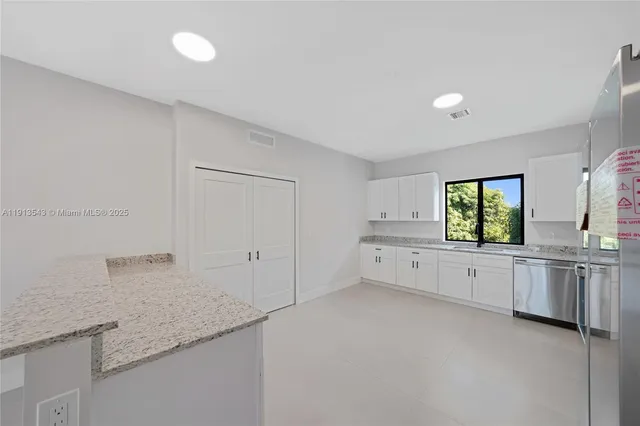 a large white kitchen with granite countertop white cabinets and white appliances