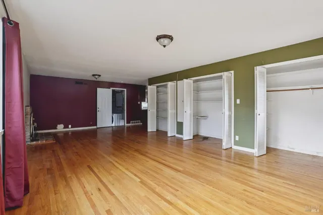 a view of an empty room with wooden floor and closet