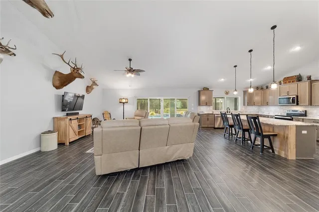 a kitchen with stainless steel appliances granite countertop a kitchen island a stove a refrigerator a sink a dining table and chairs with wooden floor