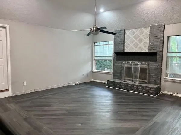 an empty room with wooden floor fireplace and windows