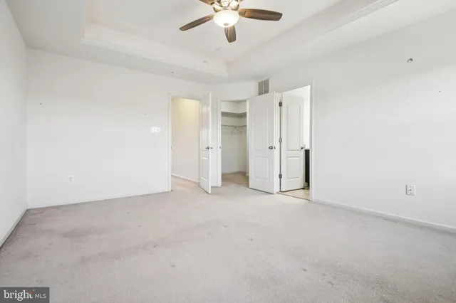 an empty room with chandelier fan and kitchen view