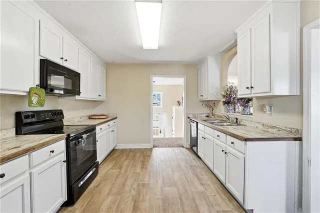 a kitchen with granite countertop a sink dishwasher stove and white cabinets with wooden floor