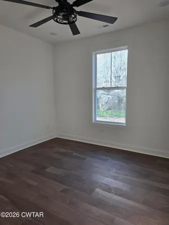 an empty room with wooden floor windows and fan