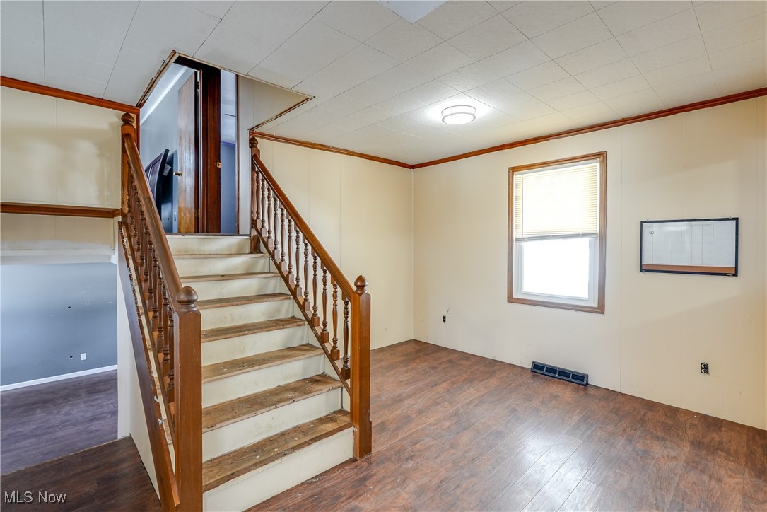 Stairs with wood-type flooring and crown molding