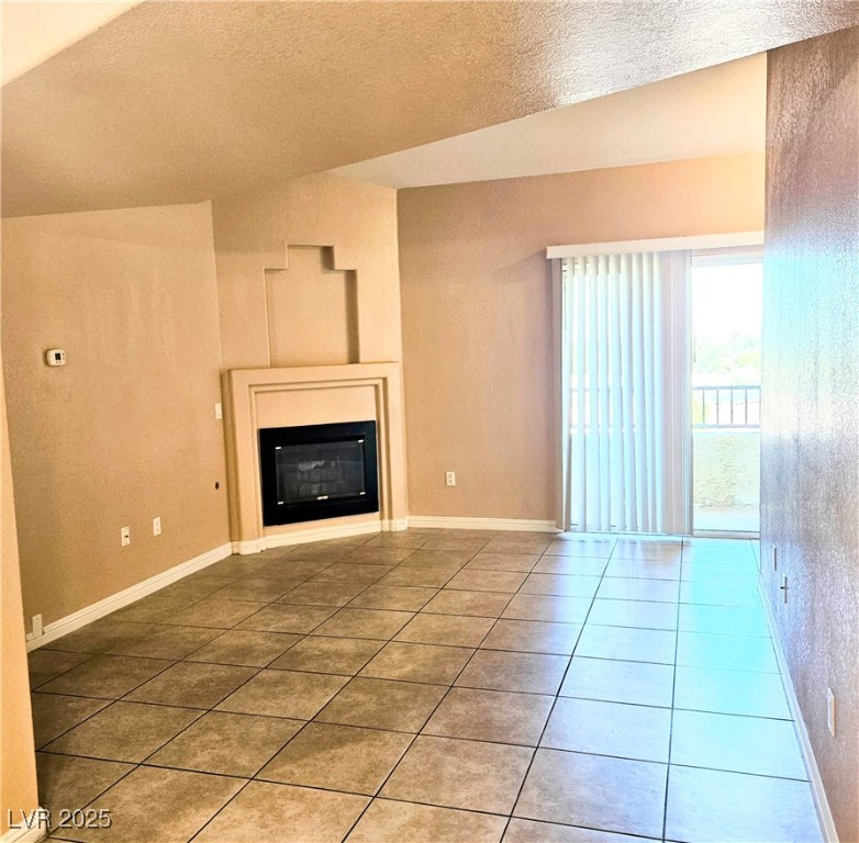 2120 Ramrod Avenue, Unit 1226 Henderson, NV 89014 - Photo 6 of 53 Unfurnished living room with lofted ceiling, a textured ceiling, a glass covered fireplace, and tile patterned floors