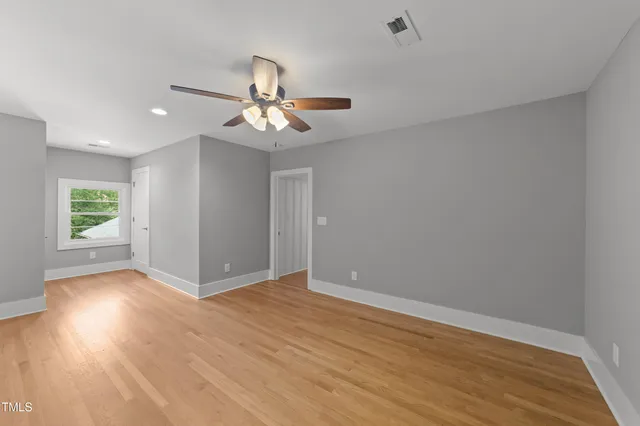 an empty room with wooden floor chandelier fan and windows