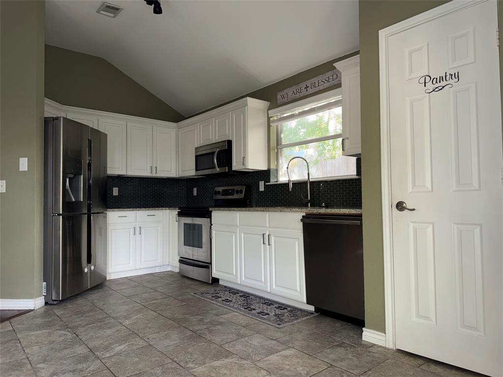 6241 Peach Tree Drive Midlothian, TX 76065 - Photo 6 of 19 Kitchen featuring white cabinetry, dark tile backsplash, stainless steel appliances, and a vaulted ceiling