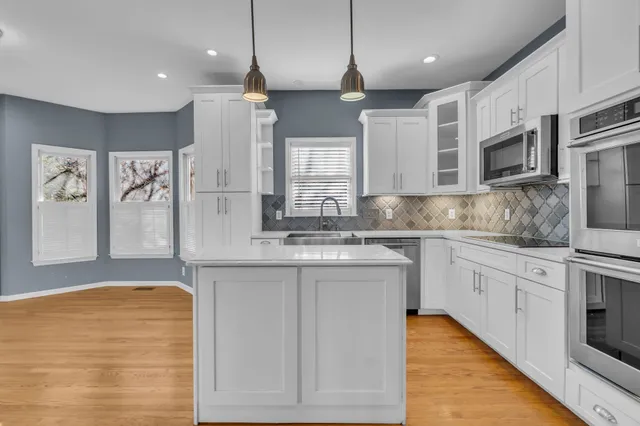 a large kitchen with stainless steel appliances granite countertop a stove a sink and white cabinets
