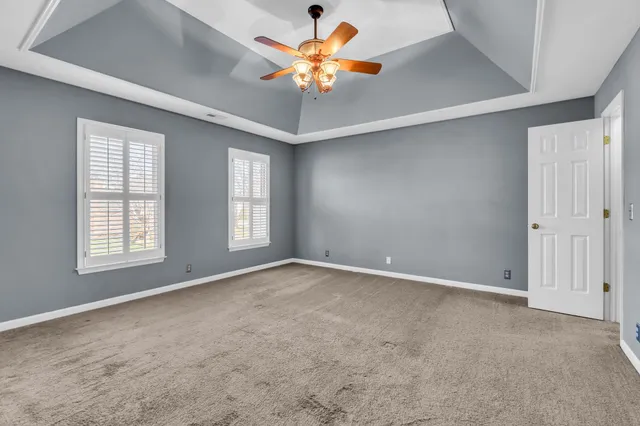 an empty room with a chandelier fan and windows