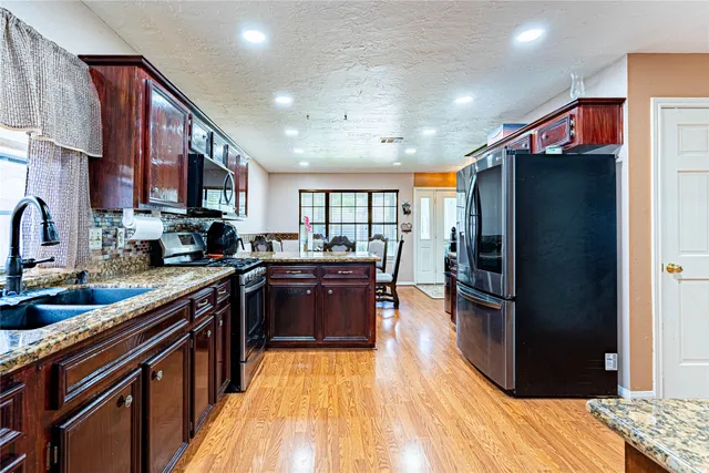 a kitchen with stainless steel appliances granite countertop a refrigerator and a wooden floors