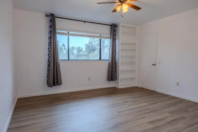 an empty room with wooden floor chandelier fan and windows
