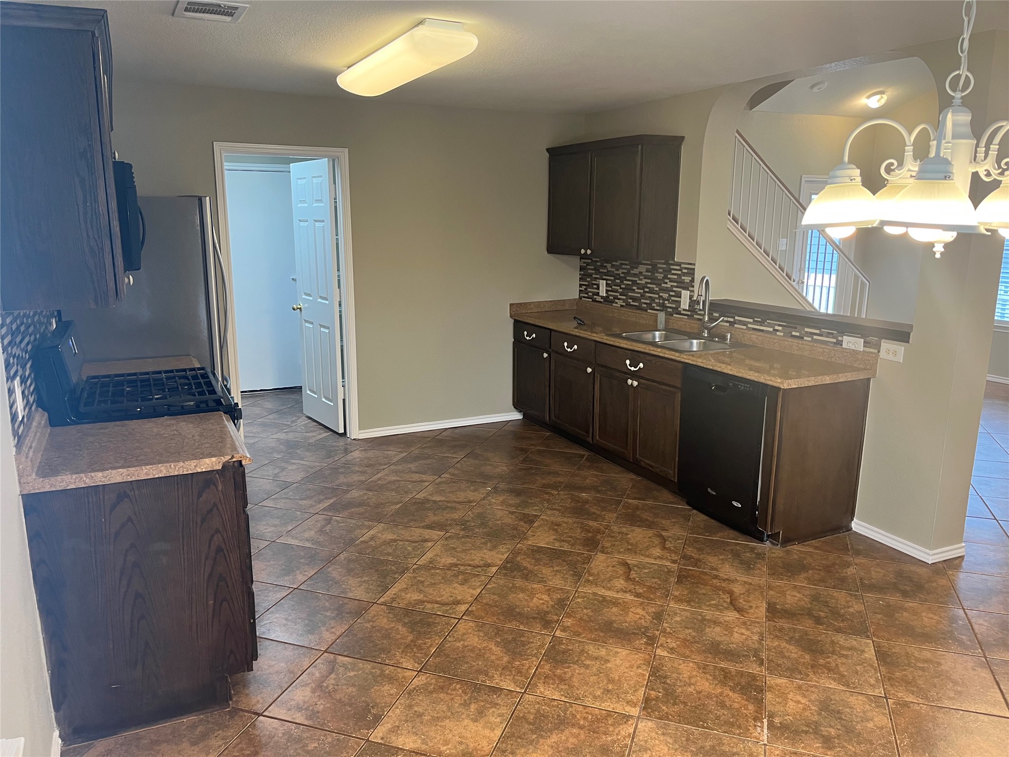 694 Hogan Kyle, TX 78640 - Photo 5 of 20 Kitchen with dark wood finish cabinetry, black dishwasher, stainless steel range with gas stovetop, backsplash, and hanging lights