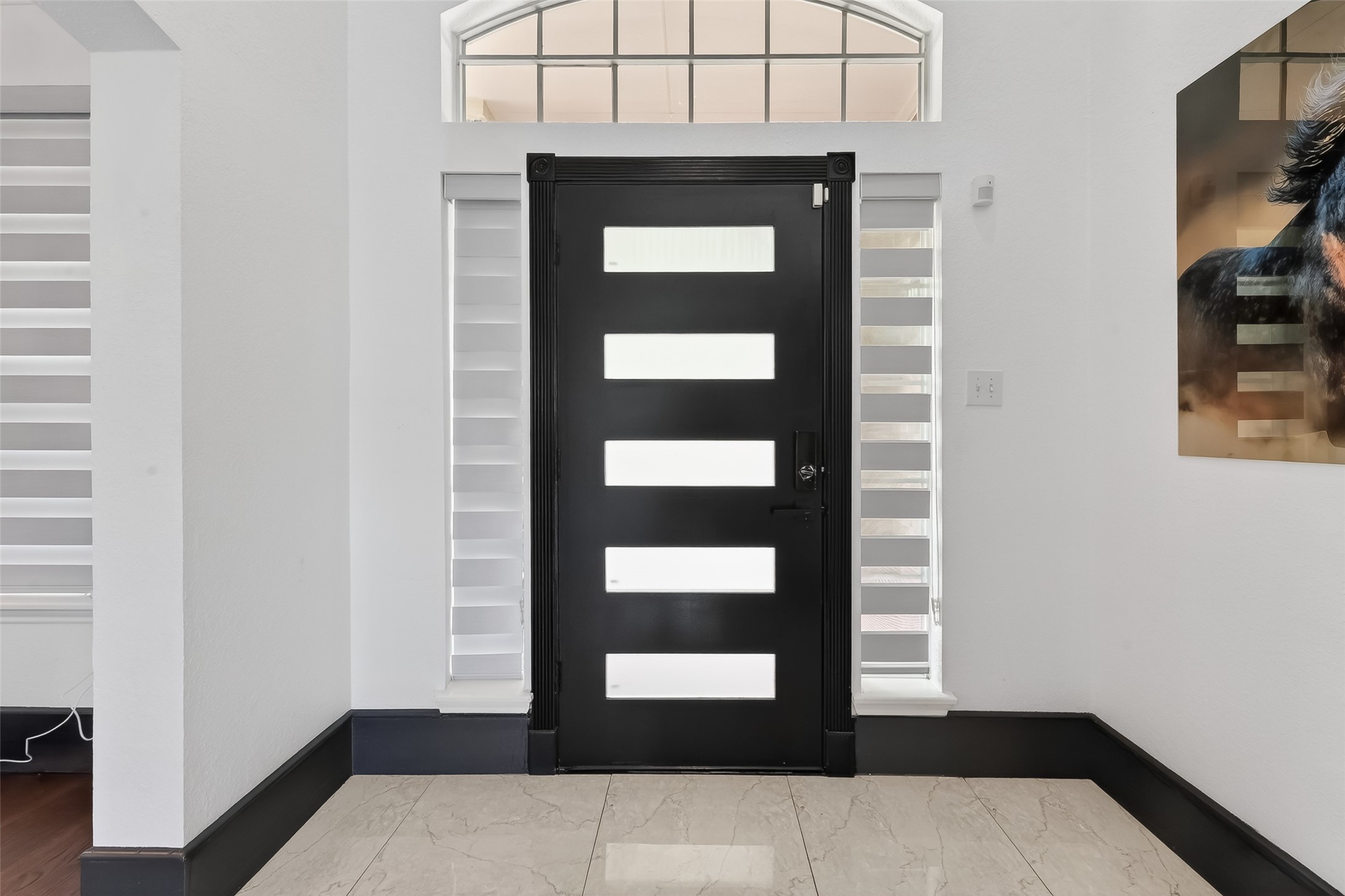1311 Rene Court Sugar Land, TX 77479 - Photo 3 of 45 This entryway features a modern black door with horizontal frosted glass panels, flanked by windows for natural light. The space has sleek white walls, black trim, and glossy marble floors, creating a contemporary and inviting atmosphere.