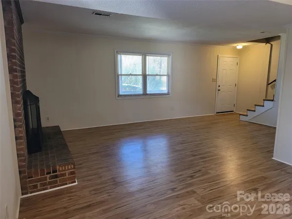 an empty room with wooden floor fireplace and windows