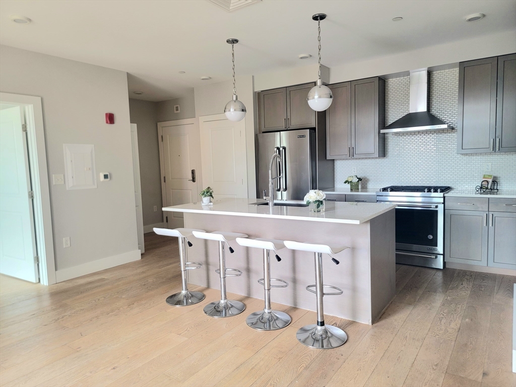 1650 Commonwealth Avenue, Unit 304A Boston, MA 02135 - Photo 7 of 26 a kitchen with stainless steel appliances granite countertop a sink a stove a refrigerator and island with wooden floor