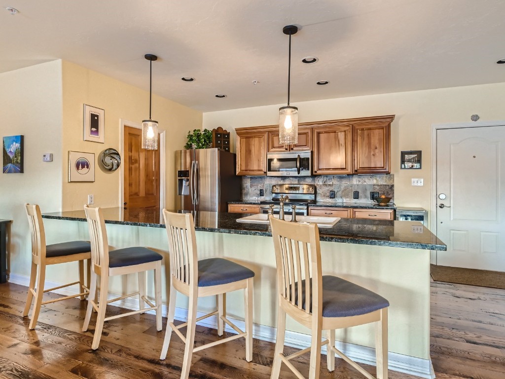 a kitchen with stainless steel appliances kitchen island granite countertop a refrigerator a stove a kitchen island and chairs with wooden floor