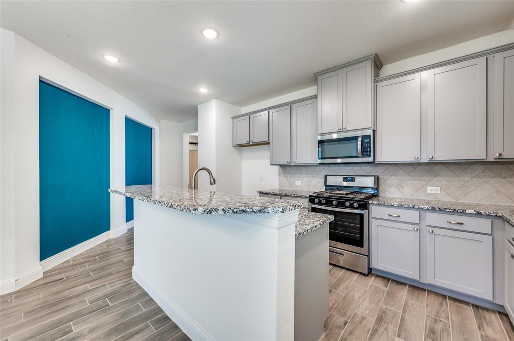 7025 Trailhead Street Little Elm, TX 76227 - Photo 11 of 25 a kitchen with stainless steel appliances granite countertop a stove a sink and a microwave