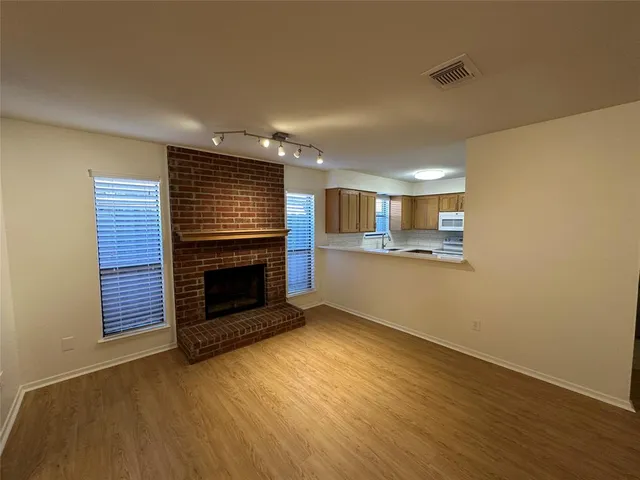 a view of an empty room with wooden floor fireplace and a window