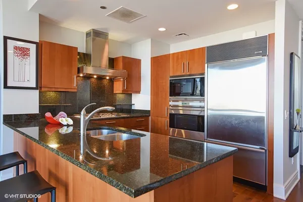a kitchen with stainless steel appliances granite countertop a refrigerator a stove and a sink with wooden floor