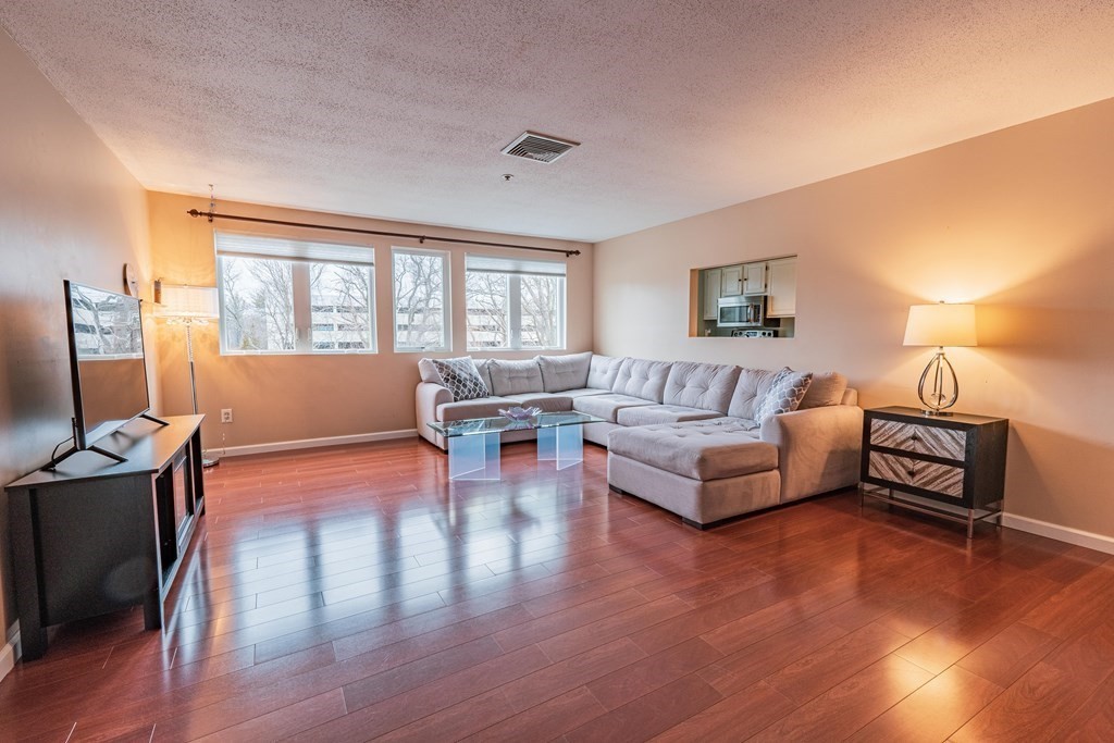 38 Dunham Road, Unit 210 Beverly, MA 01915 - Photo 5 of 30 a living room with furniture a dining table and a flat screen tv with wooden floor