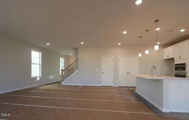 a view of an empty room with kitchen and window