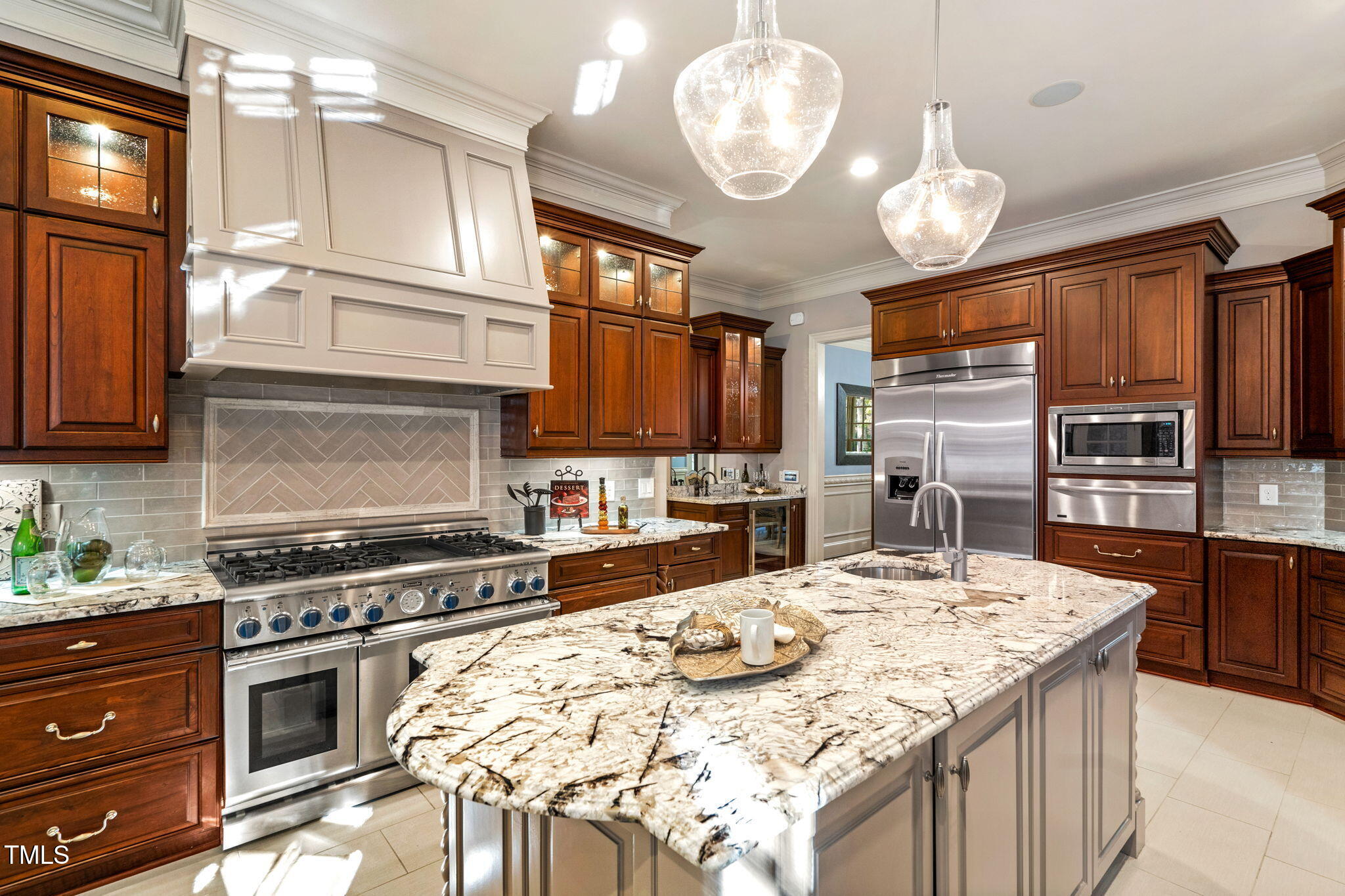11201 Jonas Ridge Lane Raleigh, NC 27613 - Photo 10 of 79 The gourmet kitchen is a true showpiece, featuring custom wood cabinetry with unique hand-detailed craftsmanship, making each piece one of a kind. Ample cabinet space is complemented by an oversized walk-in pantry and a convenient butler's pantry. The expansive island includes a vegetable sink, and high-end Thermador appliances elevate the space, including a 6-burnergas range, double ovens, a warming drawer, a built-in refrigerator, and a commercial-grade exhaust system.