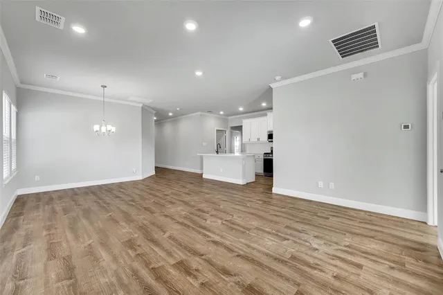 a view of an empty room with wooden floor and kitchen