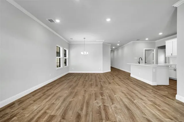a view of an empty room and kitchen with wooden floor