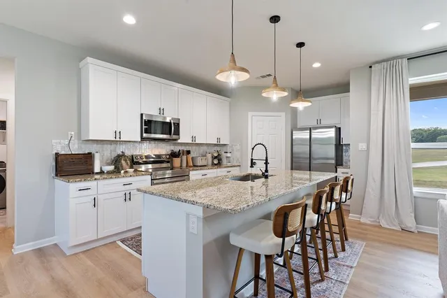 a kitchen with stainless steel appliances granite countertop a stove top oven a refrigerator a sink a dining table and chairs with wooden floor