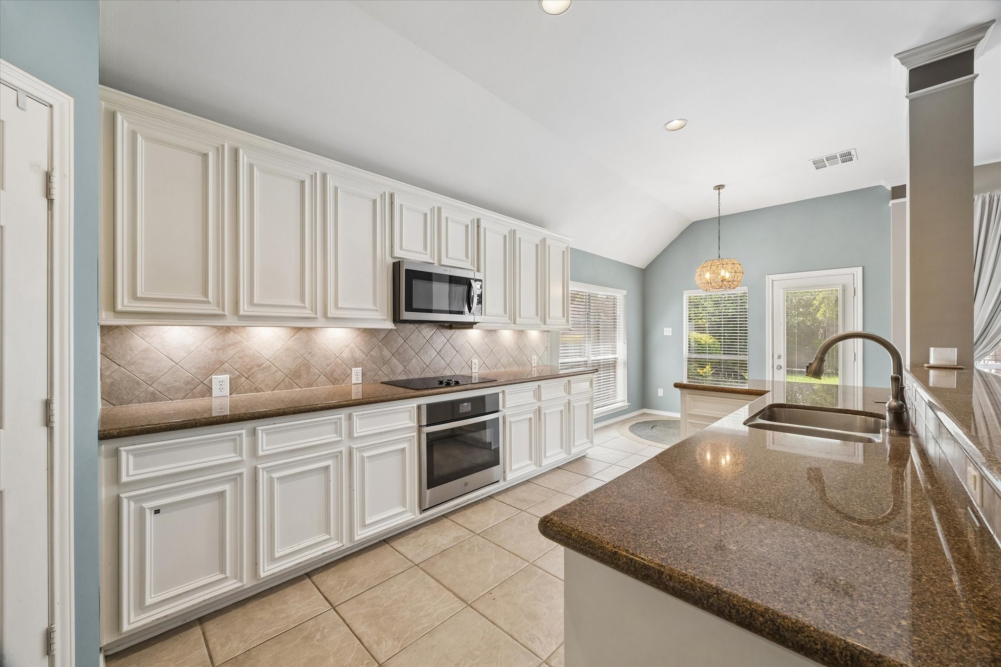 3118 Valley Court Manvel, TX 77578 - Photo 7 of 38 This kitchen features elegant white cabinetry, modern appliances, and granite countertops. The open layout includes a breakfast area with natural light from large windows and a door leading to the backyard, creating a bright and inviting space.