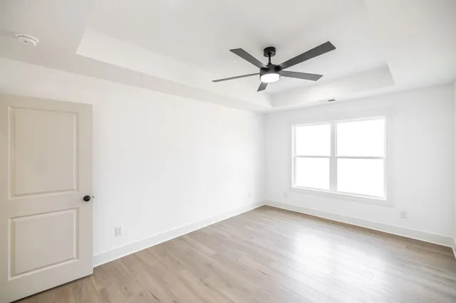 an empty room with wooden floor a ceiling fan and windows