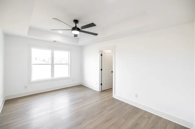 an empty room with wooden floor ceiling fan and windows
