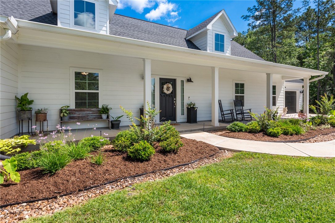 Entrance to property featuring covered porch, a shingled roof, and a yard