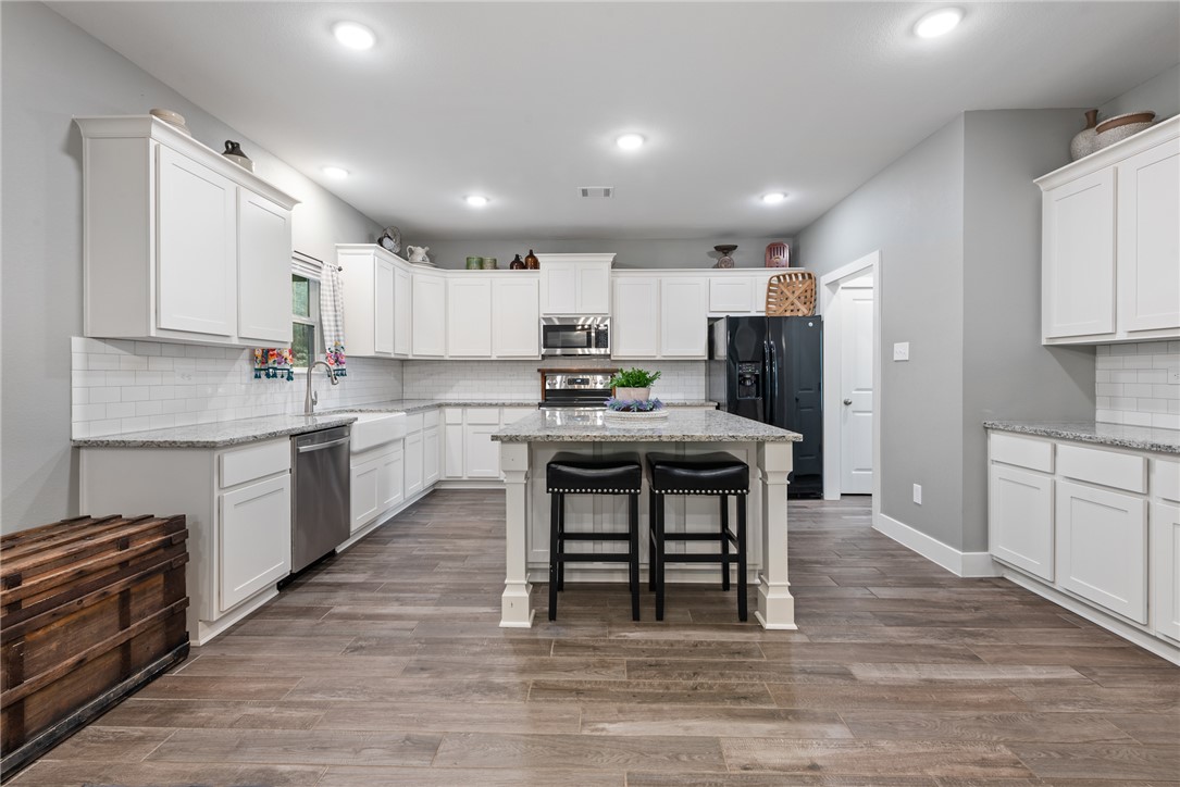 8729 Nathan Drive Waller, TX 77484 - Photo 15 of 48 Kitchen featuring appliances with stainless steel finishes, white cabinetry, decorative backsplash, a kitchen breakfast bar, and recessed lighting