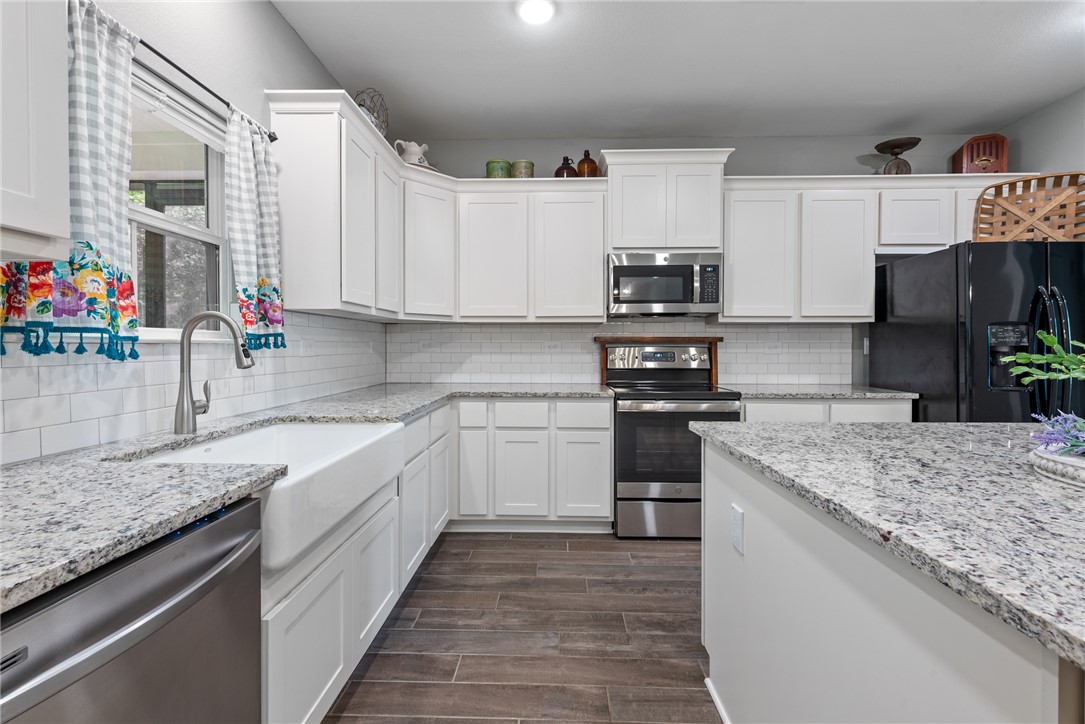 8729 Nathan Drive Waller, TX 77484 - Photo 16 of 48 Kitchen with appliances with stainless steel finishes, white cabinets, dark wood-style floors, and decorative backsplash