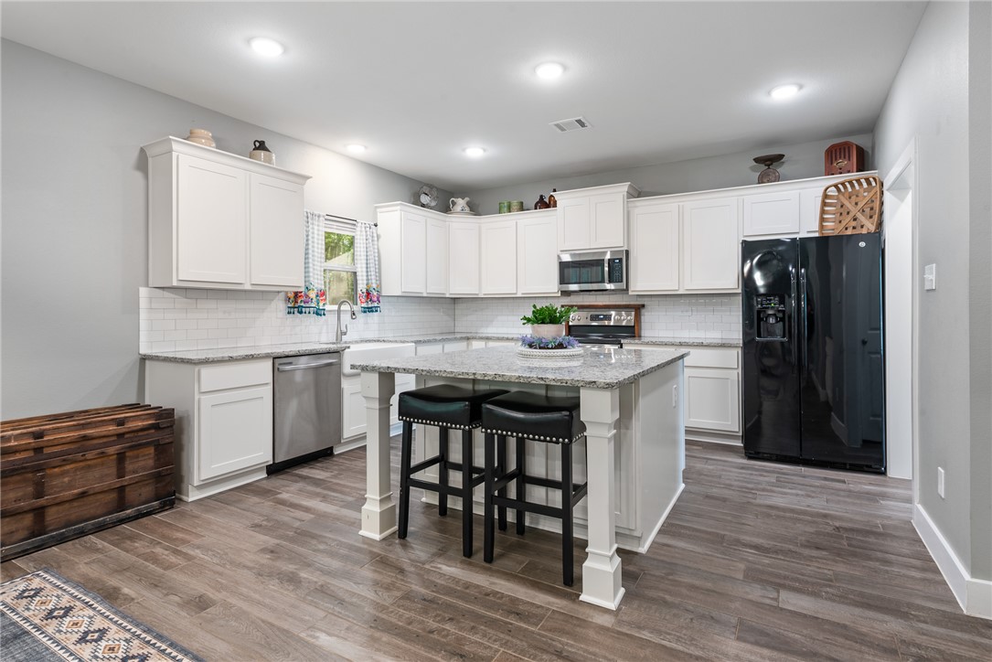 8729 Nathan Drive Waller, TX 77484 - Photo 10 of 48 Kitchen with stainless steel appliances, white cabinets, a center island, tasteful backsplash, and dark wood-style flooring