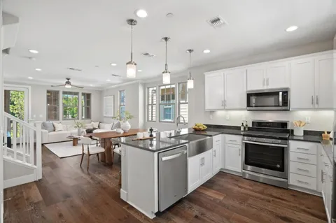 a kitchen with stainless steel appliances granite countertop a stove top oven a sink dishwasher a dining table and chairs with wooden floor