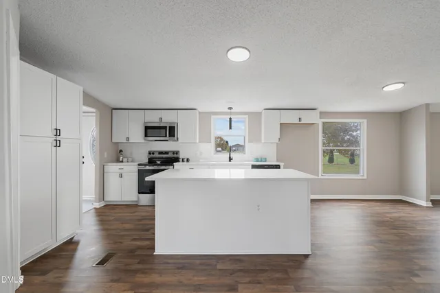 a view of kitchen with stainless steel appliances granite countertop a refrigerator oven a sink dishwasher and white cabinets with wooden floor