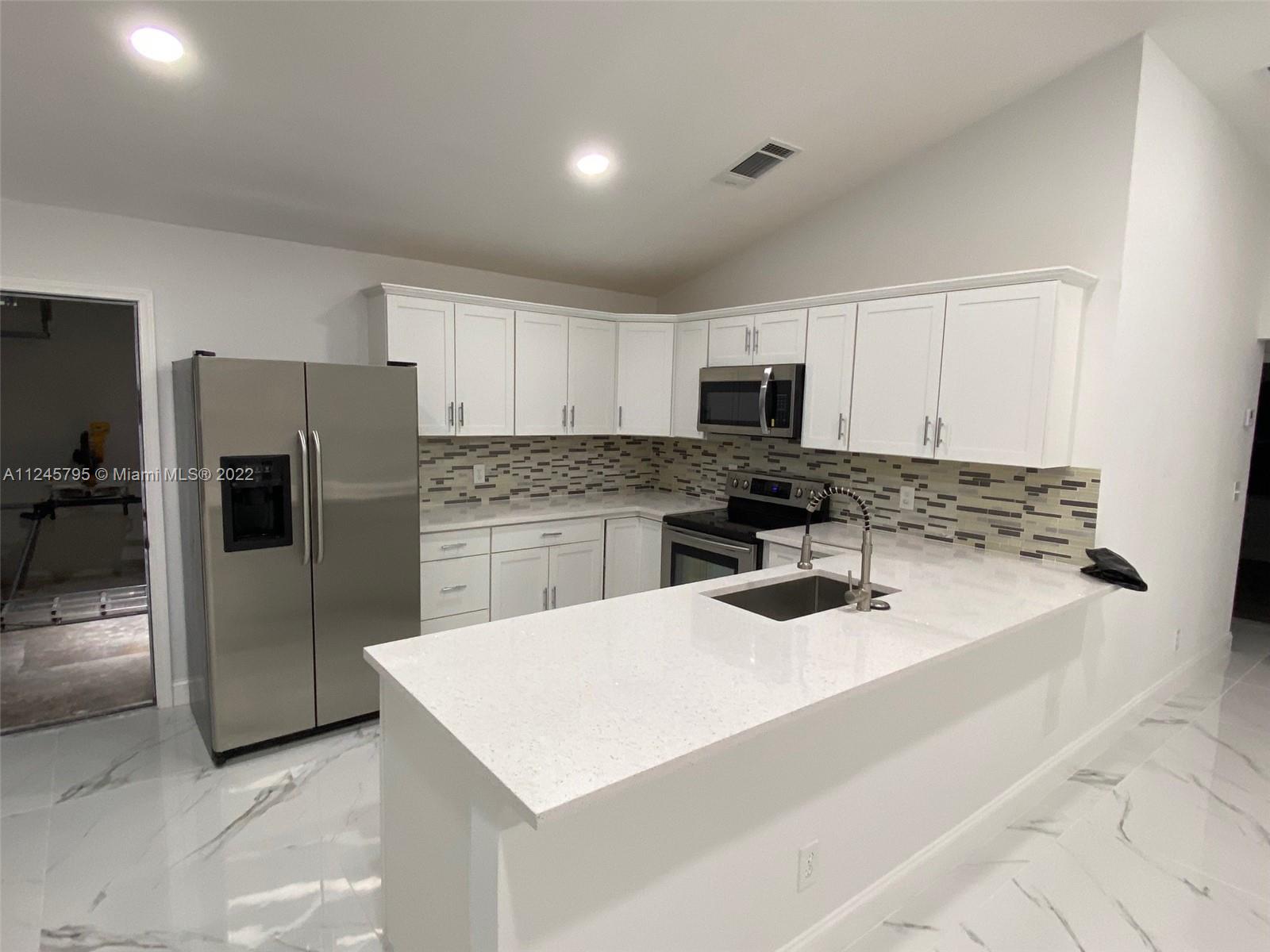 112 Raintree Trail Jupiter, FL 33458 - Photo 18 of 37 a kitchen with granite countertop a refrigerator a sink a stove top oven and stainless steel appliances