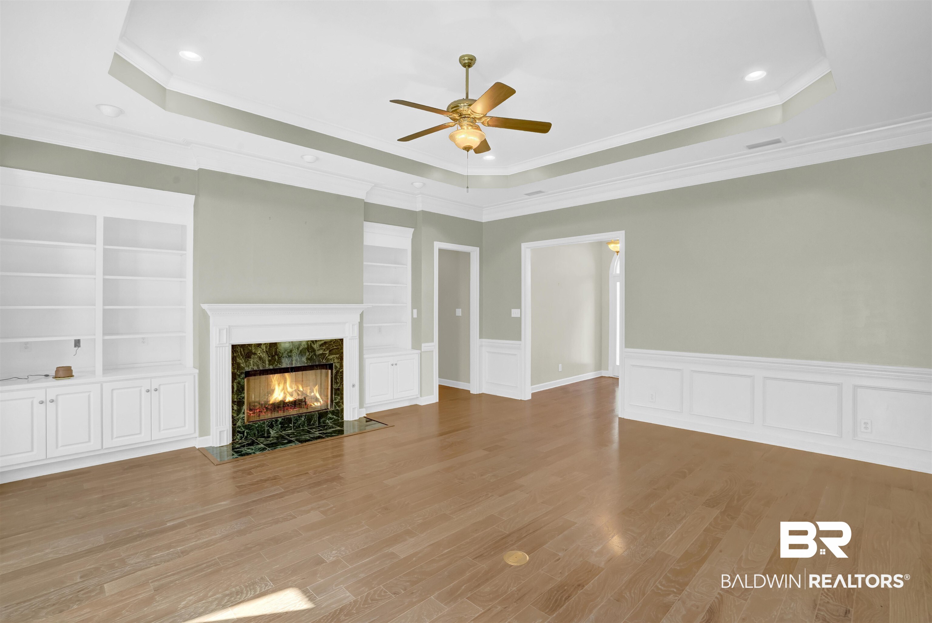111 Beaver Dam Road Fairhope, AL 36532 - Photo 8 of 51 Unfurnished living room featuring a high end fireplace, light wood-type flooring, a tray ceiling, ceiling fan, and ornamental molding