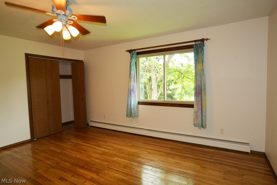 5585 Gibbs Road Andover, OH 44003 - Photo 19 of 33 Unfurnished bedroom with a baseboard heating unit, a closet, wood-type flooring, and ceiling fan