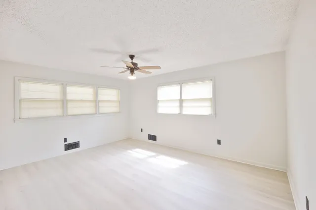 an empty room with windows and chandelier fan