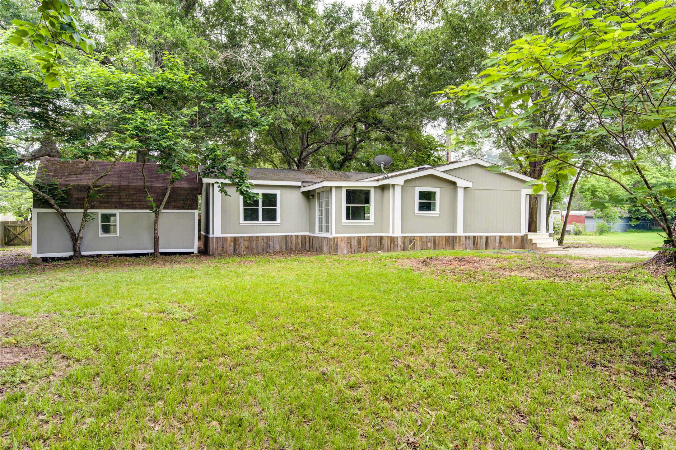 30226 Davis Street Magnolia, TX 77355 - Photo 1 of 50 This photo showcases a charming single-story home with a neutral exterior, surrounded by lush greenery and mature trees. The spacious yard offers plenty of open lawn space, perfect for outdoor activities and relaxation.