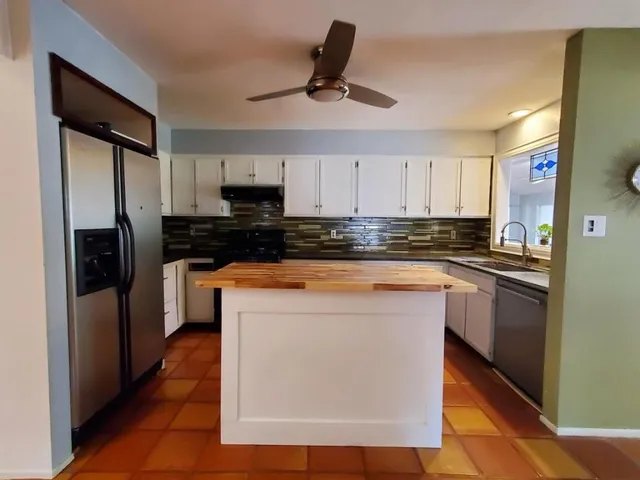 a kitchen with kitchen island granite countertop a stove top oven a sink a refrigerator and cabinets