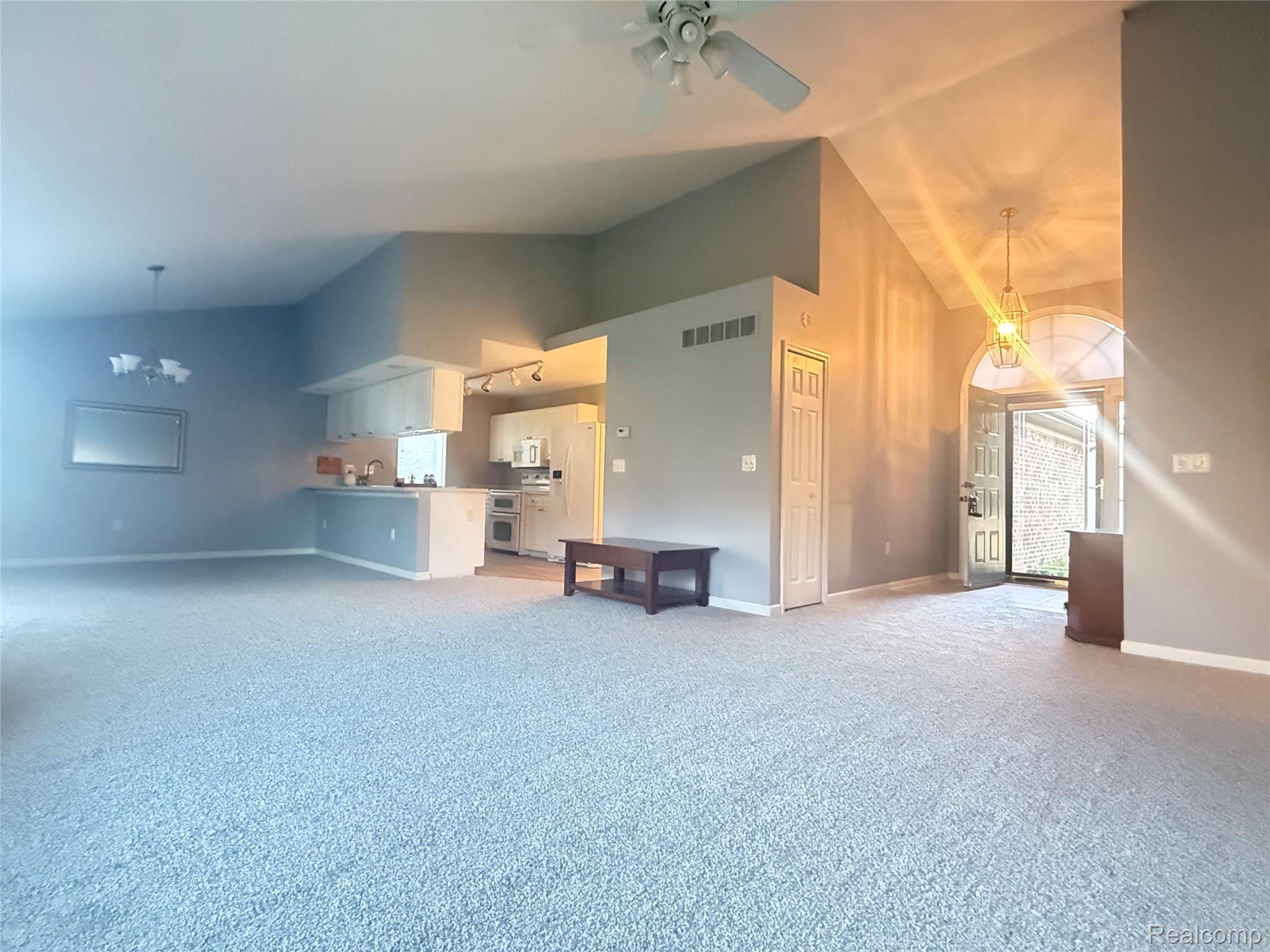 34917 Chickadee Ridge Richmond, MI 48062 - Photo 6 of 32 Open-concept living area with vaulted ceilings, a kitchen featuring white cabinetry and appliances, and a prominent arched entryway with a decorative light fixture