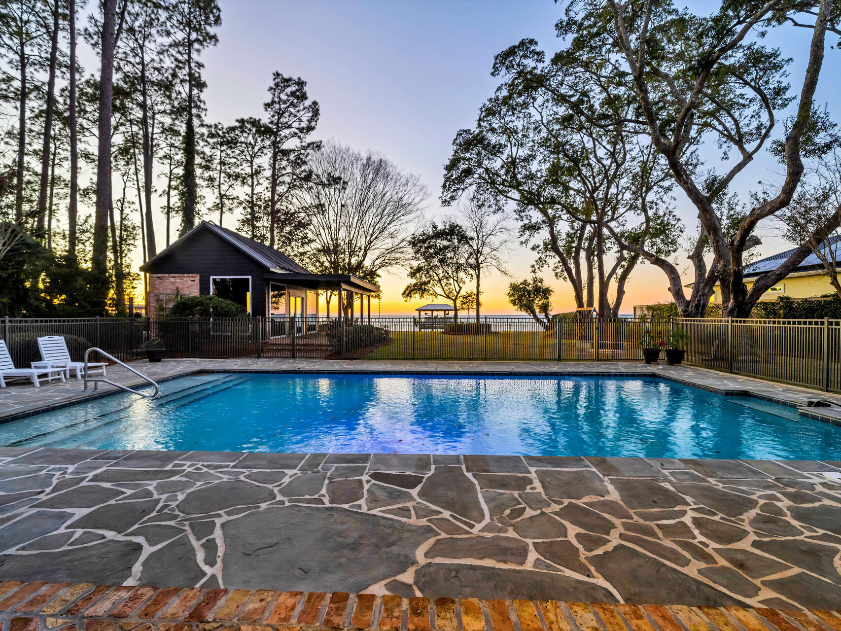 a view of swimming pool with seating space and trees in the background