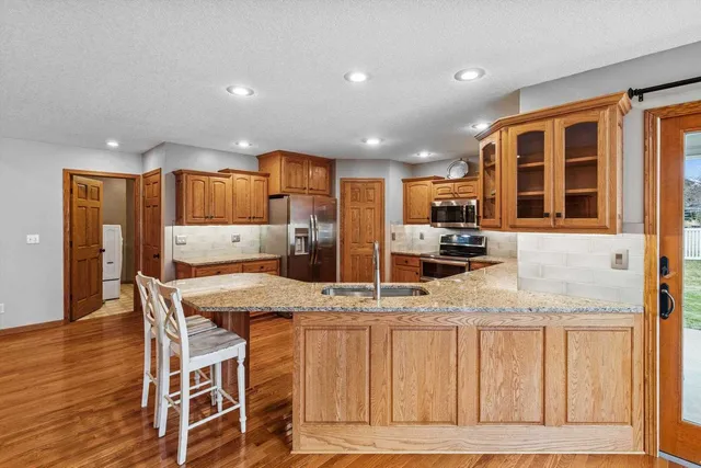 a kitchen with stainless steel appliances granite countertop a stove a sink a refrigerator with wooden cabinets and floor