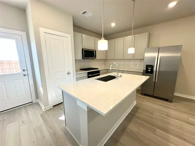 a kitchen with kitchen island a counter top space a sink a refrigerator and wooden floor